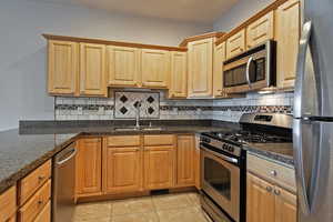 Kitchen featuring appliances with stainless steel finishes, light tile patterned flooring, and tasteful backsplash