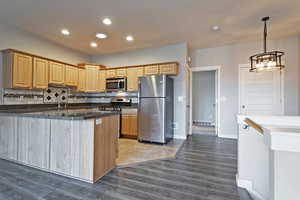 Kitchen with appliances with stainless steel finishes, a peninsula, dark wood-style floors, pendant lighting, and decorative backsplash