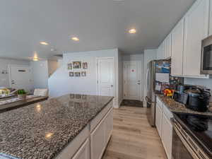 Kitchen featuring white cabinetry, dark stone counters, recessed lighting, appliances with stainless steel finishes, and light wood-style flooring