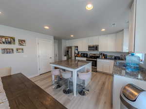 Kitchen with stainless steel appliances, a breakfast bar, dark stone counters, recessed lighting, and light wood-style flooring