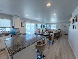 Kitchen featuring white cabinetry, dark stone counters, open floor plan, a kitchen breakfast bar, and a center island