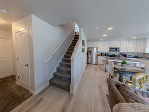 Kitchen with white cabinets, appliances with stainless steel finishes, recessed lighting, light stone countertops, and light wood-style flooring