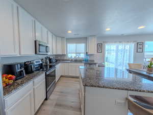 Kitchen with stainless steel appliances, dark stone counters, a center island, white cabinets, and a textured ceiling
