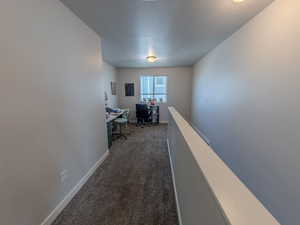 Corridor featuring an office area, dark colored carpet, and a textured ceiling