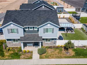View of front of home with a shingled roof, stone siding, covered porch, and a fenced backyard