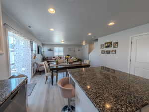 Kitchen featuring dark stone countertops, stainless steel dishwasher, a breakfast bar, recessed lighting, and open floor plan