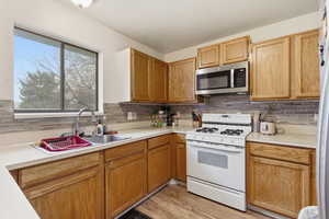 Kitchen featuring white gas stove, light countertops, stainless steel microwave, and backsplash