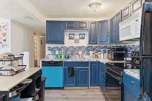 Kitchen with black / electric stove, white microwave, dishwashing machine, freestanding refrigerator, and light wood-style floors