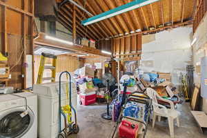 Miscellaneous room with unfinished concrete flooring, washing machine and dryer, water heater, and vaulted ceiling