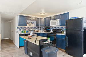 Kitchen with freestanding refrigerator, electric range oven, blue cabinets, white microwave, and backsplash