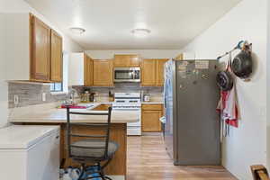 Kitchen featuring a kitchen bar, light countertops, appliances with stainless steel finishes, brown cabinets, and a peninsula