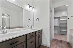 Full bathroom featuring double vanity, a spacious closet, a stall shower, and dark wood-style flooring