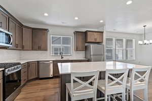 Kitchen with stainless steel appliances, a kitchen bar, light stone countertops, a center island, and dark wood-type flooring