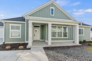 View of front of home with board and batten siding, covered porch, and roof with shingles