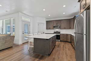 Kitchen featuring stainless steel appliances, a kitchen bar, a center island, dark wood finished floors, and backsplash