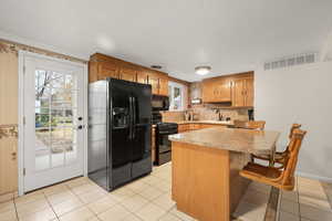 Kitchen featuring black appliances, light countertops, a peninsula, a kitchen breakfast bar, and brown cabinets