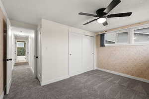 Unfurnished bedroom featuring a textured ceiling, a closet, dark colored carpet, ceiling fan, and multiple windows