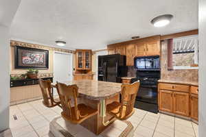 Kitchen featuring a textured ceiling, black appliances, brown cabinets, a breakfast bar area, and a center island
