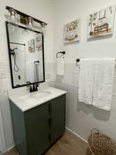 Full bathroom with vanity, wood finished floors, a wainscoted wall, tile walls, and a shower