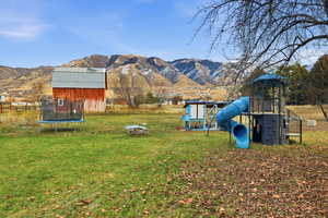 View of green lawn featuring a trampoline, a mountain view, and a playground