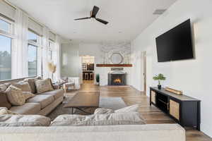 Living room featuring a ceiling fan, wood finished floors, and a large fireplace