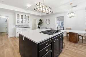 Kitchen with dark cabinets, a center island, hanging light fixtures, and white cabinetry