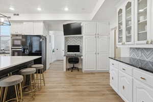 Kitchen with dark stone countertops, a kitchen bar, white cabinets, black refrigerator with ice dispenser, and recessed lighting