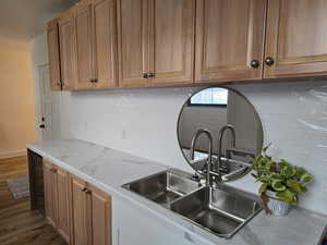 Kitchen with brown cabinetry, beverage cooler, light stone counters, dark wood-style flooring, and decorative backsplash