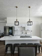 Kitchen with dark wood-type flooring, white cabinetry, tile counters, a center island, and a textured ceiling