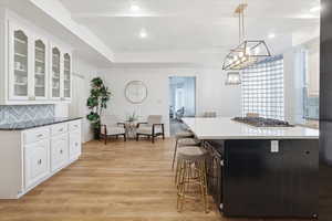Kitchen featuring backsplash, white cabinets, pendant lighting, light wood finished floors, and glass insert cabinets