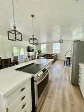 Kitchen with tile countertops, stainless steel appliances, white cabinetry, pendant lighting, and a textured ceiling