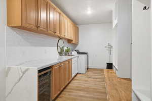 Kitchen with light stone counters, wine cooler, decorative backsplash, light wood-style flooring, and washing machine and clothes dryer