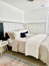 Carpeted bedroom featuring a decorative wall, a wainscoted wall, and a textured ceiling
