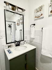 Full bath with vanity, tile walls, a shower with curtain, and wainscoting