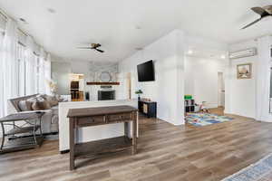 Living room featuring ceiling fan, a stone fireplace, light wood-style flooring, and a wall mounted air conditioner