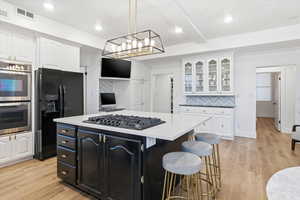 Kitchen featuring dark cabinets, a center island, black appliances, decorative backsplash, and a breakfast bar area