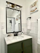 Bathroom with vanity, a shower with shower curtain, tile walls, and wainscoting