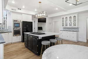 Kitchen featuring backsplash, dark cabinets, dark stone counters, light wood finished floors, and recessed lighting