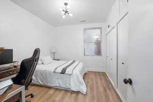 Bedroom featuring light wood-style floors, a desk, a chandelier, and two closets