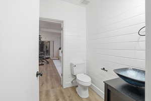 Half bathroom with light wood finished floors, wood walls, and vanity