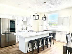 Kitchen with smart refrigerator, a kitchen bar, a center island, hanging light fixtures, and a textured ceiling