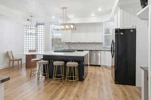 Kitchen with white cabinetry, freestanding refrigerator, pendant lighting, a center island, and backsplash