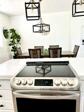 Kitchen view of tile counters, electric stove, a chandelier, a textured ceiling, and decorative light fixtures