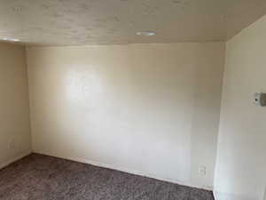 Carpeted empty room with a textured ceiling and baseboards