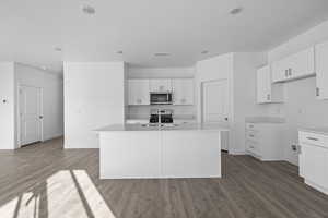 Kitchen featuring white cabinetry, appliances with stainless steel finishes, a kitchen island with sink, dark wood-style floors, and light stone countertops