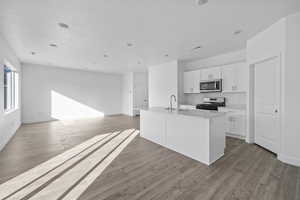 Kitchen featuring a center island with sink, white cabinetry, range with gas stovetop, light wood-type flooring, and stainless steel microwave