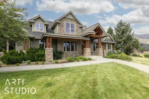 Craftsman-style house featuring a front lawn, a standing seam roof, covered porch, and stone siding