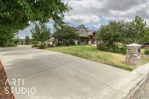 View of front facade featuring stone siding, a front lawn, concrete driveway, and covered porch