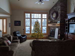 Living area featuring a stone fireplace, a ceiling fan, lofted ceiling, and carpet