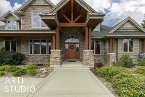 Doorway to property with stone siding, covered porch, and a shingled roof